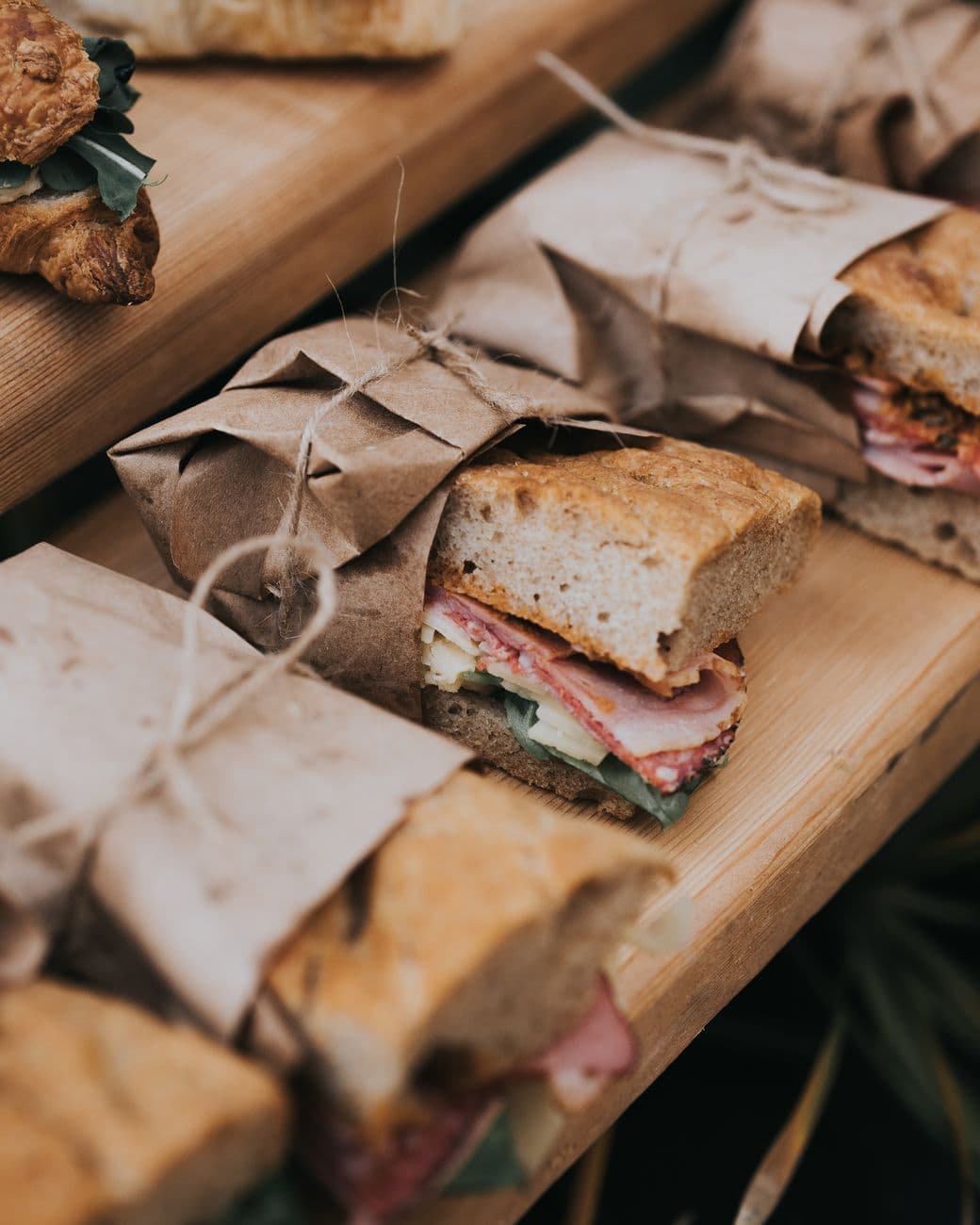 Sandwiches garnis emballés dans du papier kraft et ficelés, alignés sur une planche